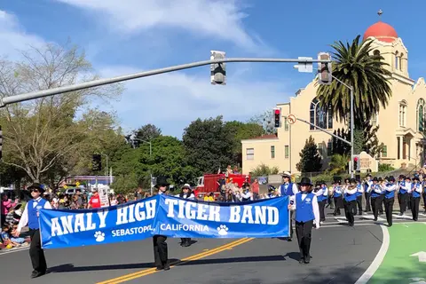 A high school marching band carrying a banner in a street parade.