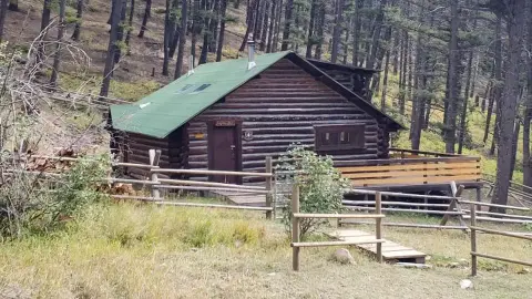A log cabin surrounded by trees and a wooden fence.
