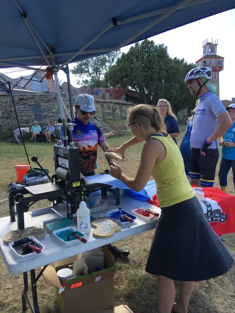 People at a printing demonstration table outdoors under a tent.