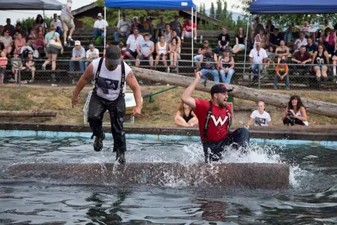 Two competitors log rolling in a pool with spectators watching from bleachers.