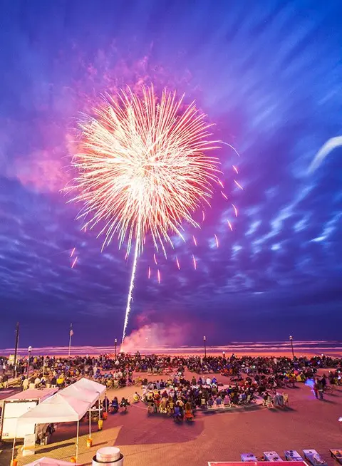 A large firework explodes over a crowd gathered at night.