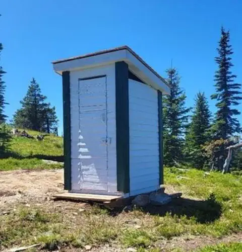 An outdoor outhouse stands in a mountainous landscape.