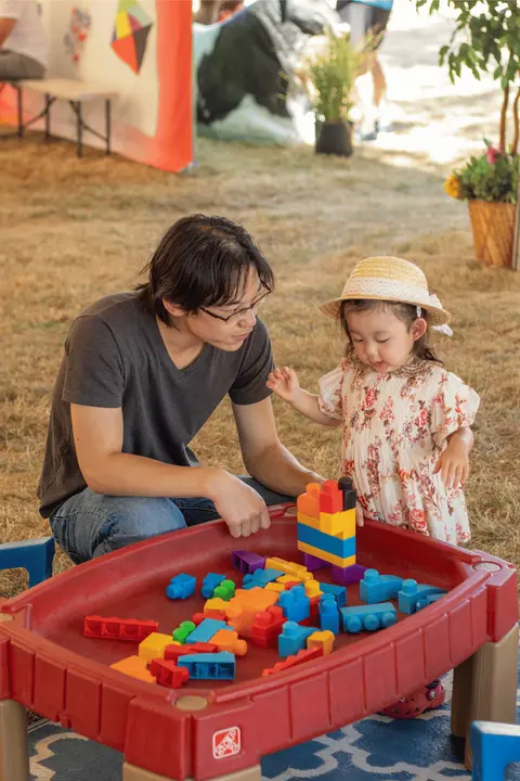 An adult and a toddler play with plastic building blocks outside.