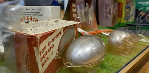 A photograph showing vintage potato baking containers and boxes on display inside a case.