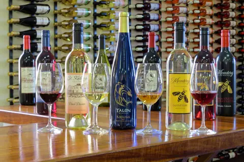 Wine bottles and wine glasses are arranged on a wooden counter in front of a wine rack.