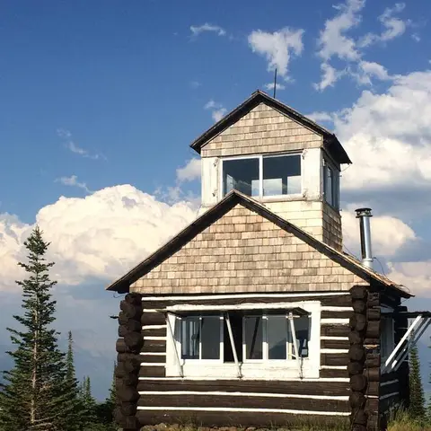 A log cabin structure with a lookout tower under a partly cloudy sky.