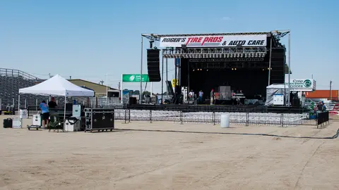 An outdoor stage set up on a dirt field with a banner and sound equipment.