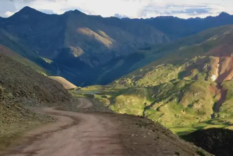 A winding dirt road cuts through a scenic mountainous landscape.