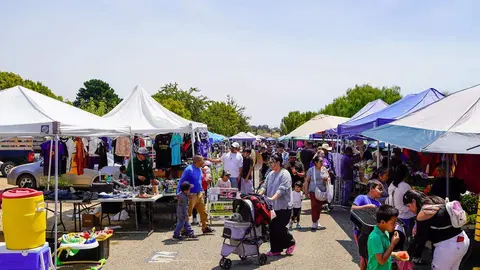 People shop at an outdoor market with numerous tents and merchandise displays.