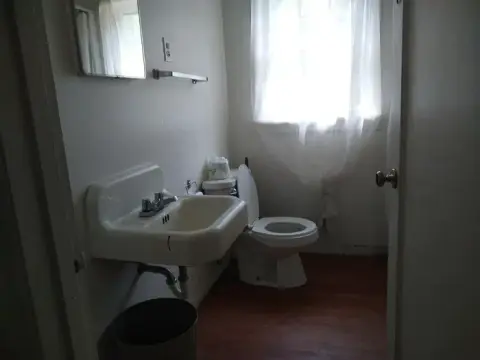 A small bathroom with a sink, toilet, and window with white curtains.