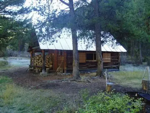 A rustic log cabin stands in a wooded area among trees.