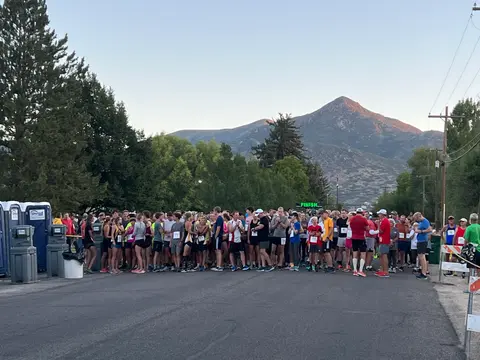 A large group of runners gathers on a street before a race, with a mountain in the background.