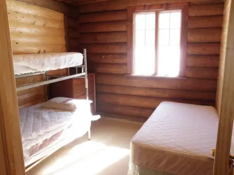 An interior view of a log cabin bedroom with bunk beds and a single bed.
