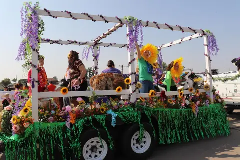 A parade float decorated with flowers and greenery carrying people and animals.