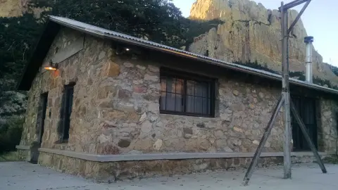 A stone building sits before rocky mountains.