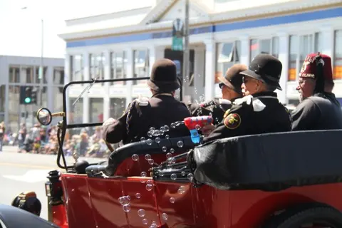 A red vintage car carries people in a parade.