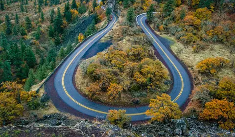 An aerial view of a winding mountain road with hairpin turns surrounded by autumn foliage.