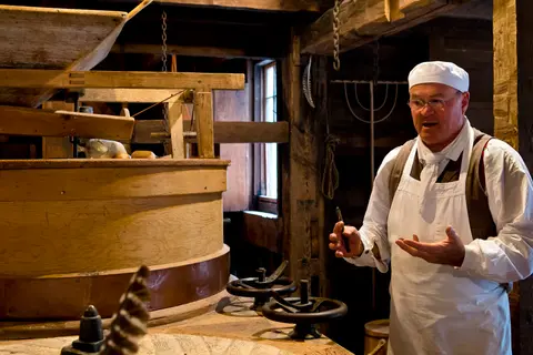A man in historic attire stands inside a mill next to milling equipment.