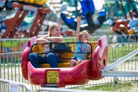 Two children ride an amusement park ride with a warning sign on the car.