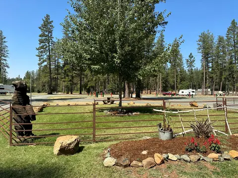 A fenced area with a carved wooden bear sculpture and trees in a campground.