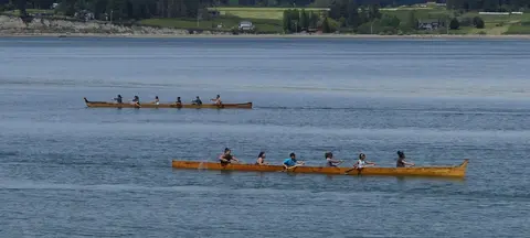Two wooden canoes with people paddling are on a body of water.