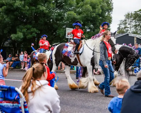 People ride horses decorated with patriotic tinsel in a parade.