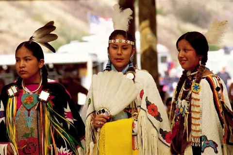 Three young women in traditional regalia are participating in an event.