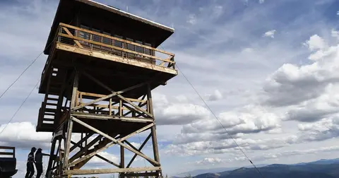 A tall wooden fire lookout tower stands under a cloudy sky.