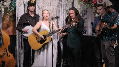 A band performs on stage with instruments including a guitar, fiddle, and banjo.