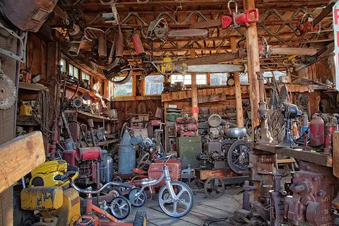An interior view of a cluttered workshop filled with tools, engines, and equipment.