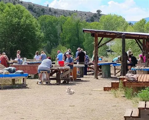 People at outdoor work tables with a dog resting on the ground.