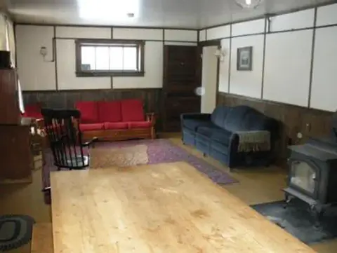An interior shot of a rustic room featuring a wooden table, couches, and a wood stove.