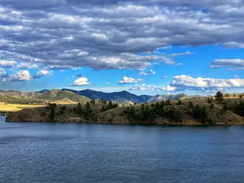 A scenic view of a body of water with hills, mountains, and a cloudy sky.