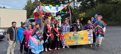A group of people posing outdoors next to a colorful parade float holding a banner.