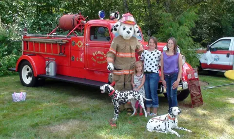 People and dogs pose in front of a red fire truck with a mascot.