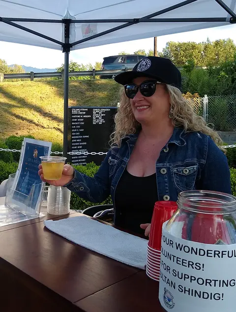 A woman serves a drink at an outdoor bar beneath a tent.