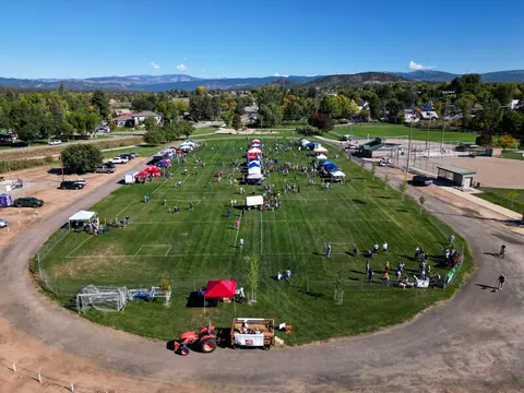 An aerial view shows an outdoor event on a large sports field with tents and people.