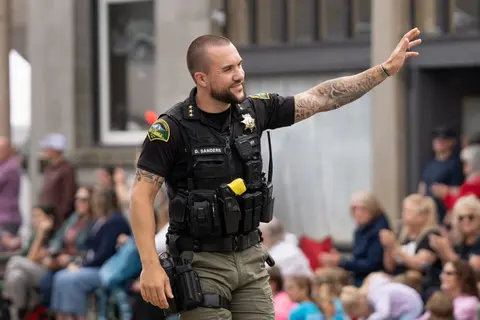 A sheriff in uniform waving to a crowd during an outdoor event.