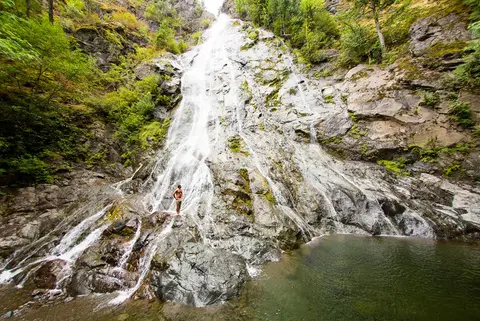 A large waterfall flows down a steep rocky cliff into a pool of water.