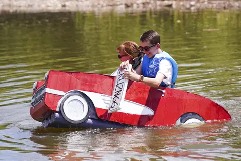 People in a homemade cardboard car boat on the water.