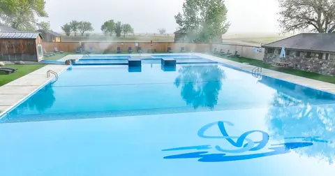 An outdoor swimming pool complex with steaming water surrounded by buildings.