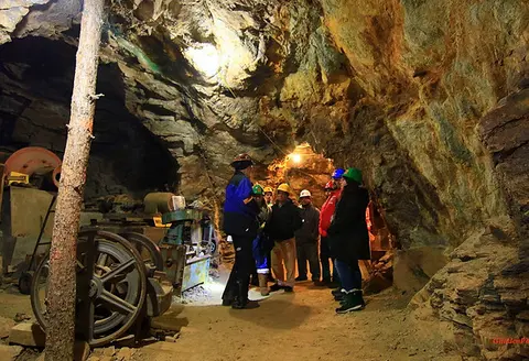 A group of people wearing hard hats explore the interior of a rocky mine.