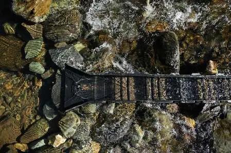 A sluice box rests in a stream among rocks and rushing water.