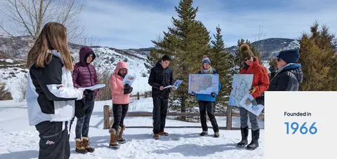 A group of people holding maps in a snowy outdoor area.