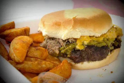 A burger with cheese and green chile served with potato wedges.