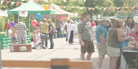 People walking along a street market with booths and balloons.