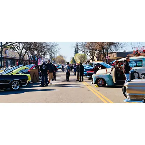 A street lined with classic cars and people attending an outdoor car show.