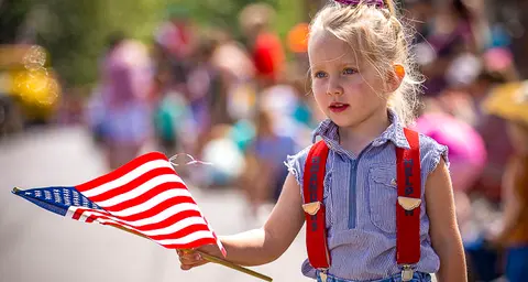 A young girl holds a small American flag at an outdoor event.
