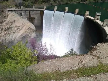 Water spills over the crest of a large dam.