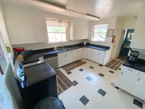 An interior shot of a kitchen with white cabinets, black countertops, and a stove in the foreground.